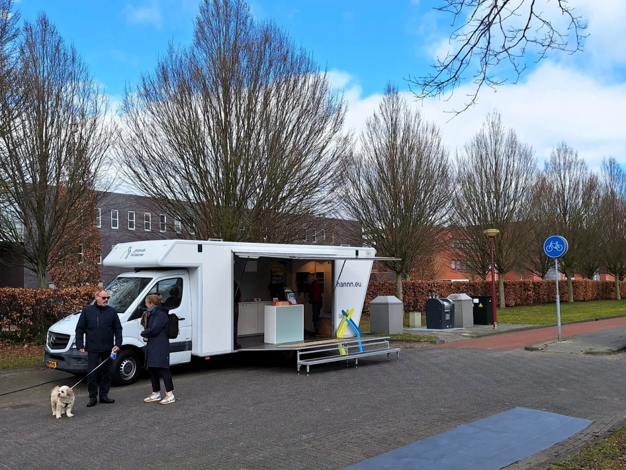 De Gezonde Huiskamer op afstand met twee mensen ervoor staand in gesprek met een hondje en de Smart Floor uitgerold op de straat