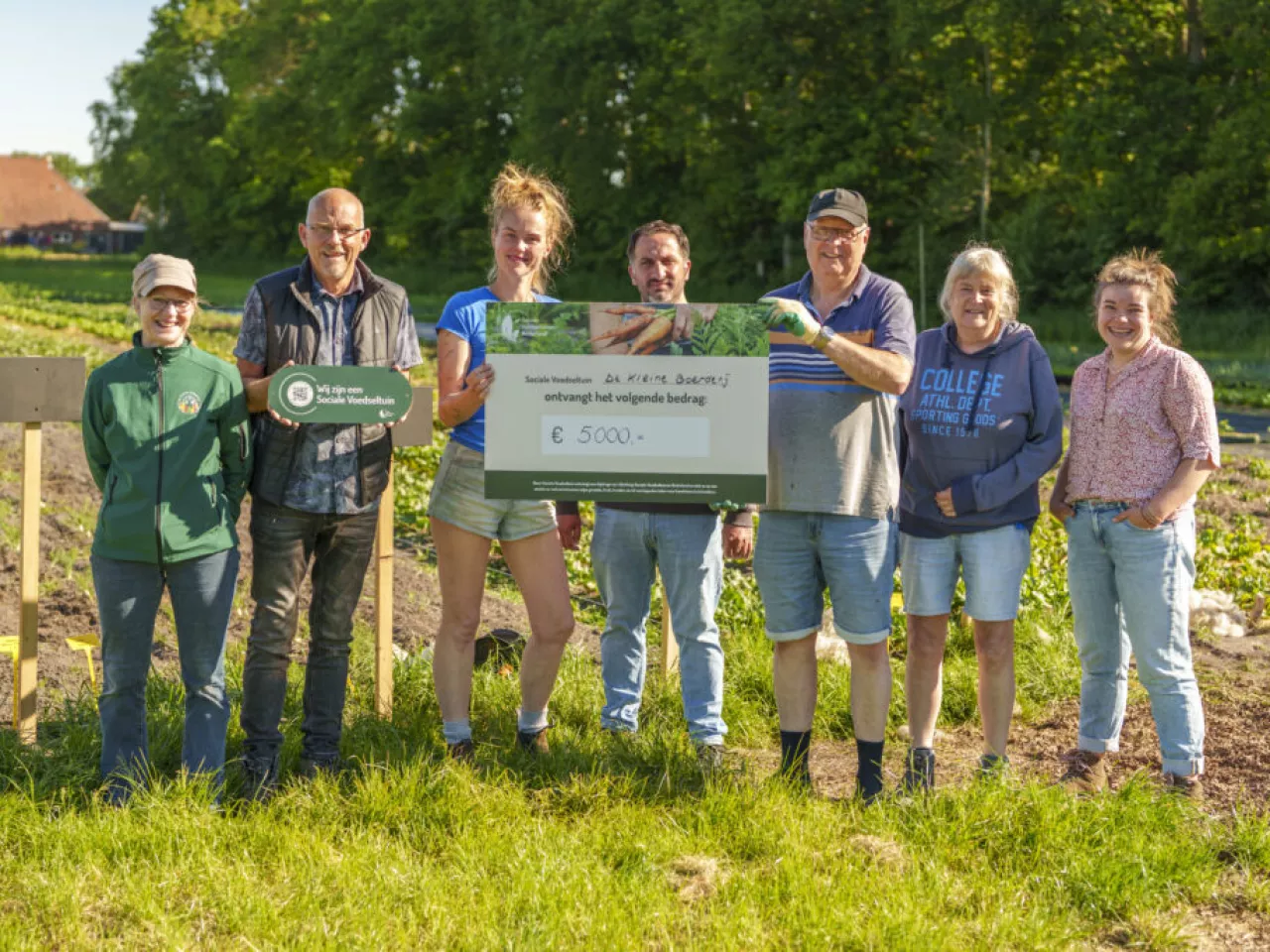 Zeven mensen van De Kleine Boerderij op een rij met een cheque in handen